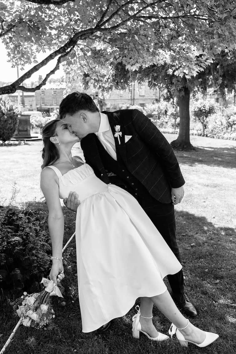 Black and white photo of a bride and groom sharing a romantic kiss outdoors under a tree in Bakewell taken by 21 Photography