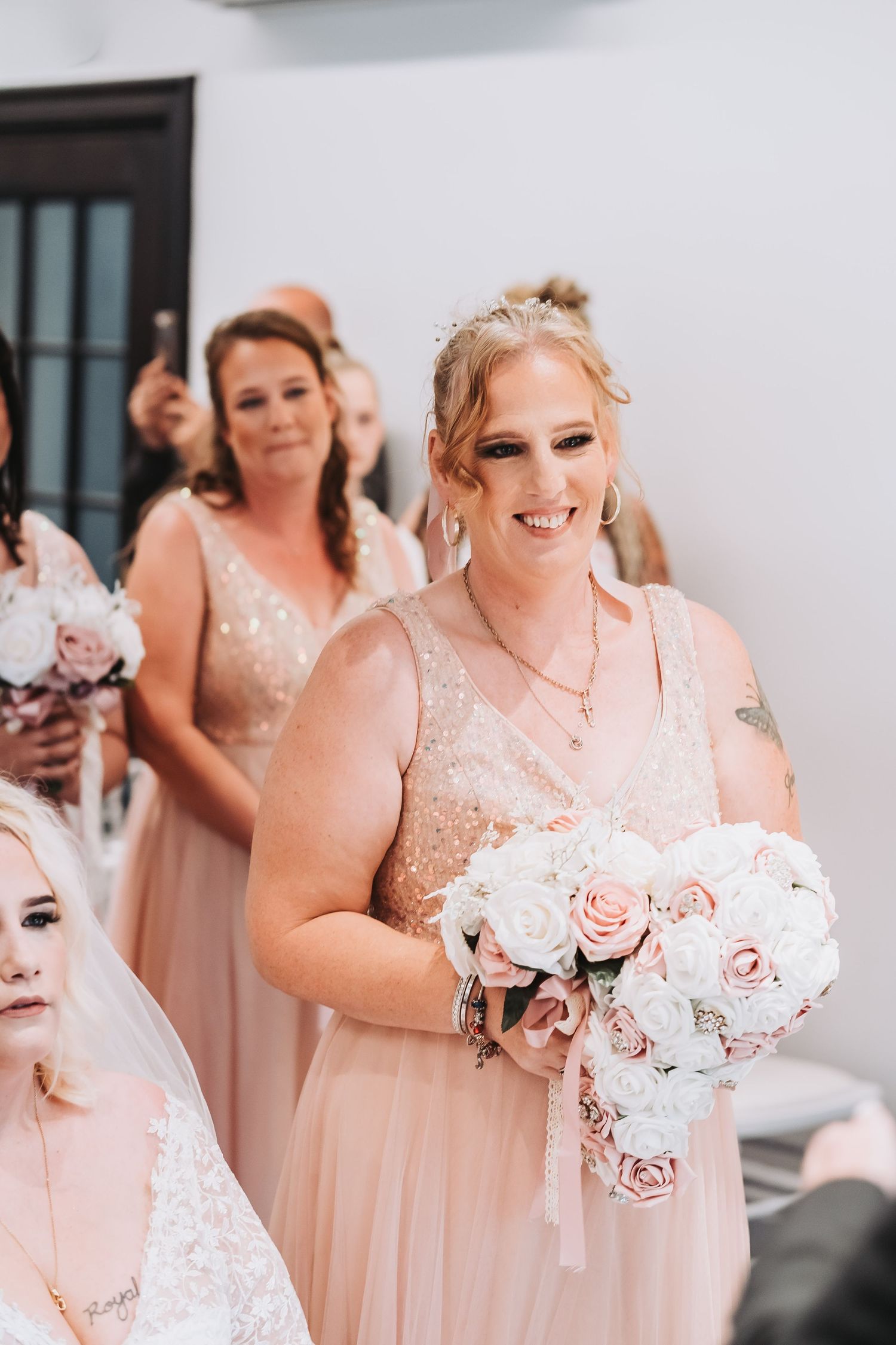 Wedding party in blush pink dresses holding white and pink rose bouquets.