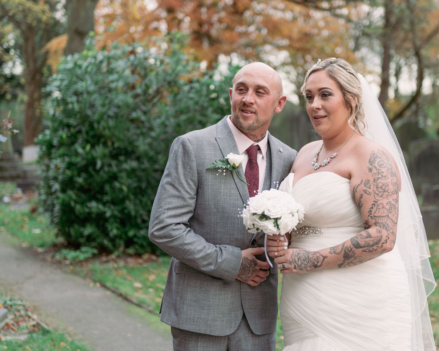 Wedding couple poses together with bride in white dress and groom in grey suit.