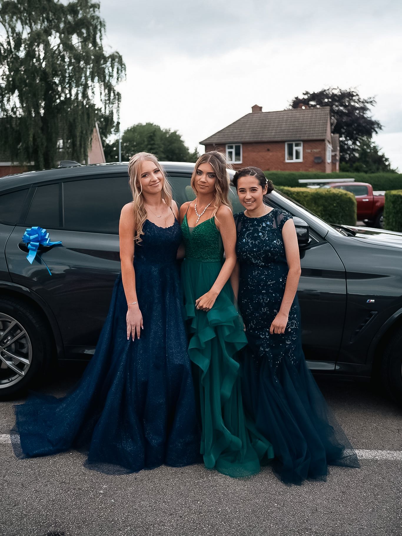 Three people in elegant evening gowns posing together next to car.