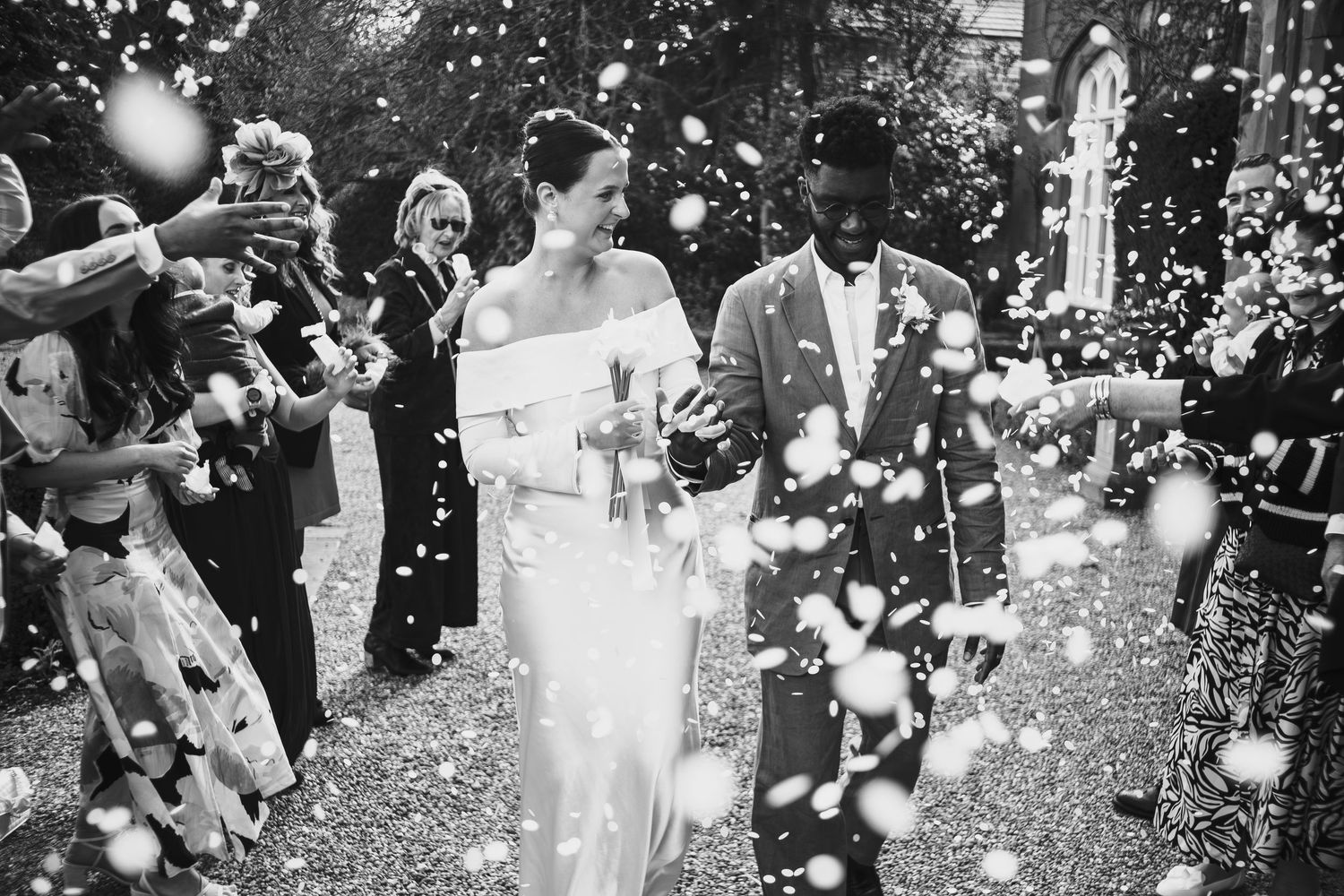 Black and white wedding photo of bride and groom walking through confetti shower surrounded by cheering guests  at dunston hall estate