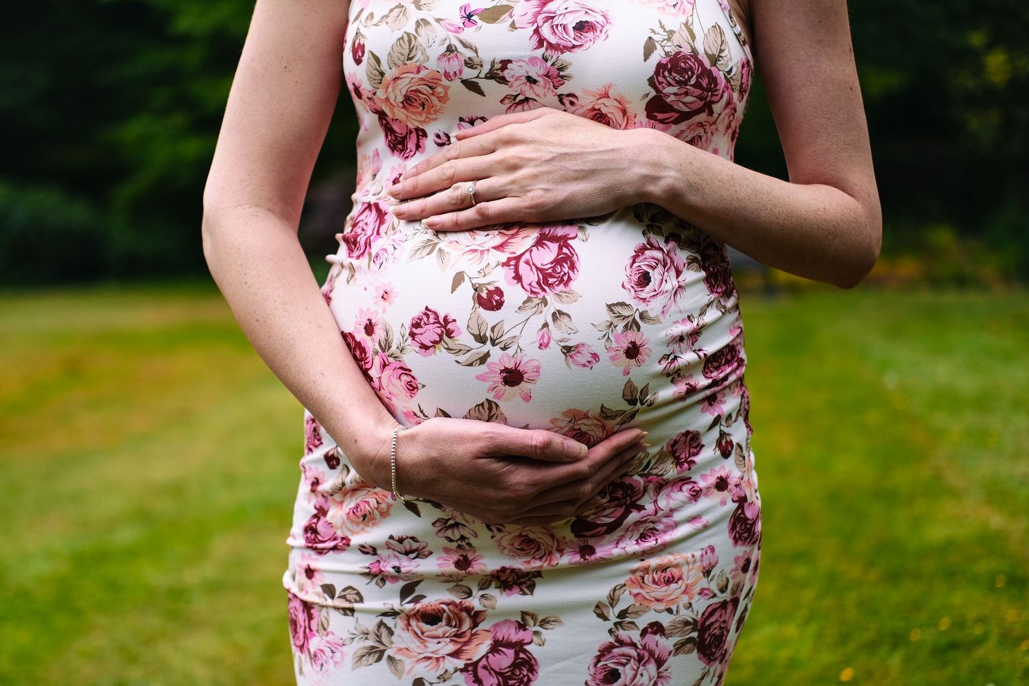 Close-up shots of a floral maternity dress showing pregnancy details in a garden setting.