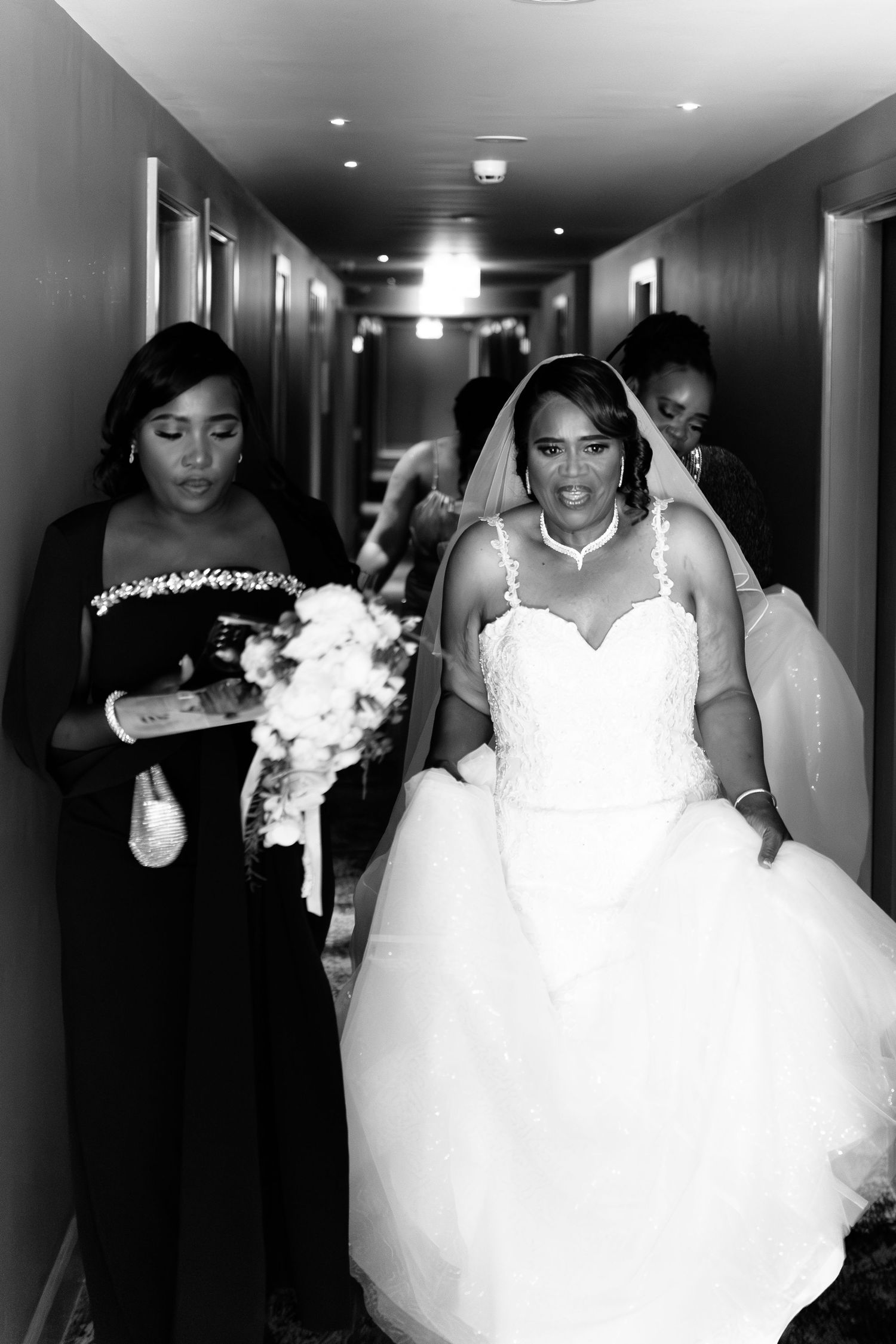 Black and white photo of a bride walking down a hallway with her bridesmaid at Wildes Inn, Chesterfield taken by 21 Photography