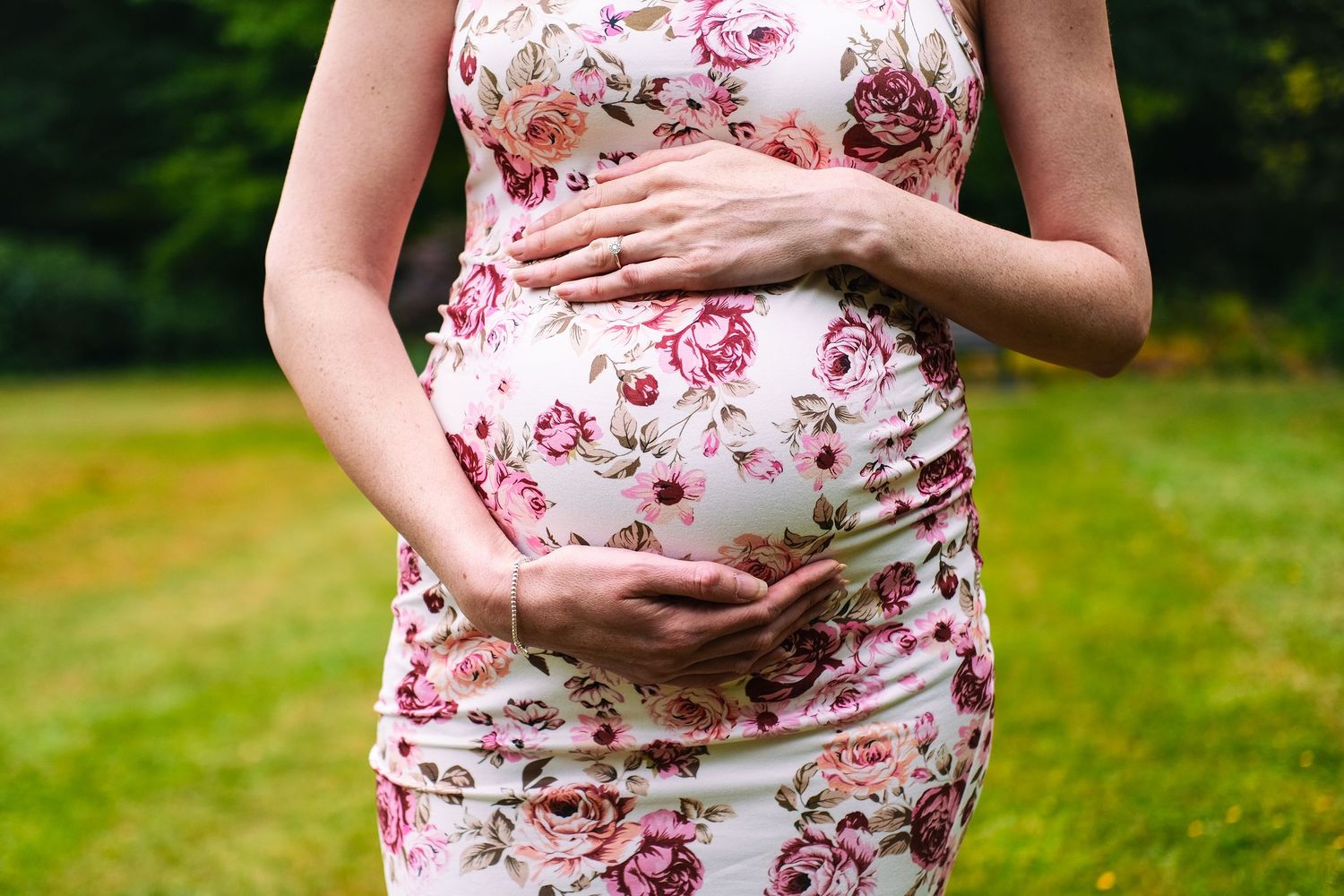 A close-up shot of hands cradling a pregnant belly in a floral pink dress.