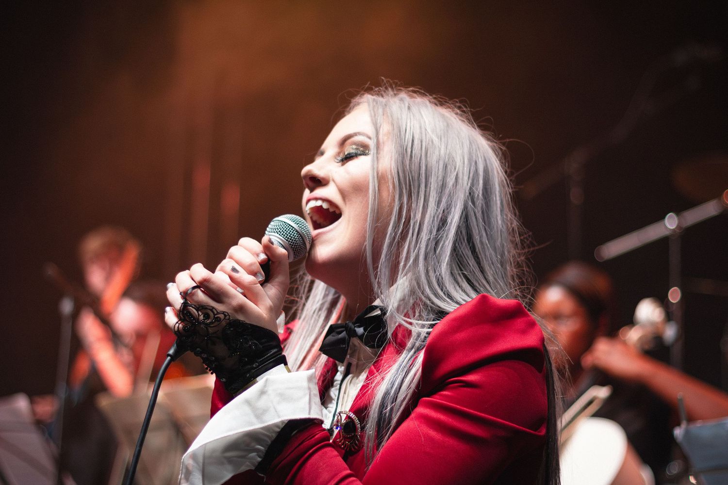 Singer in red jacket performing passionately on stage with microphone under dramatic lighting.