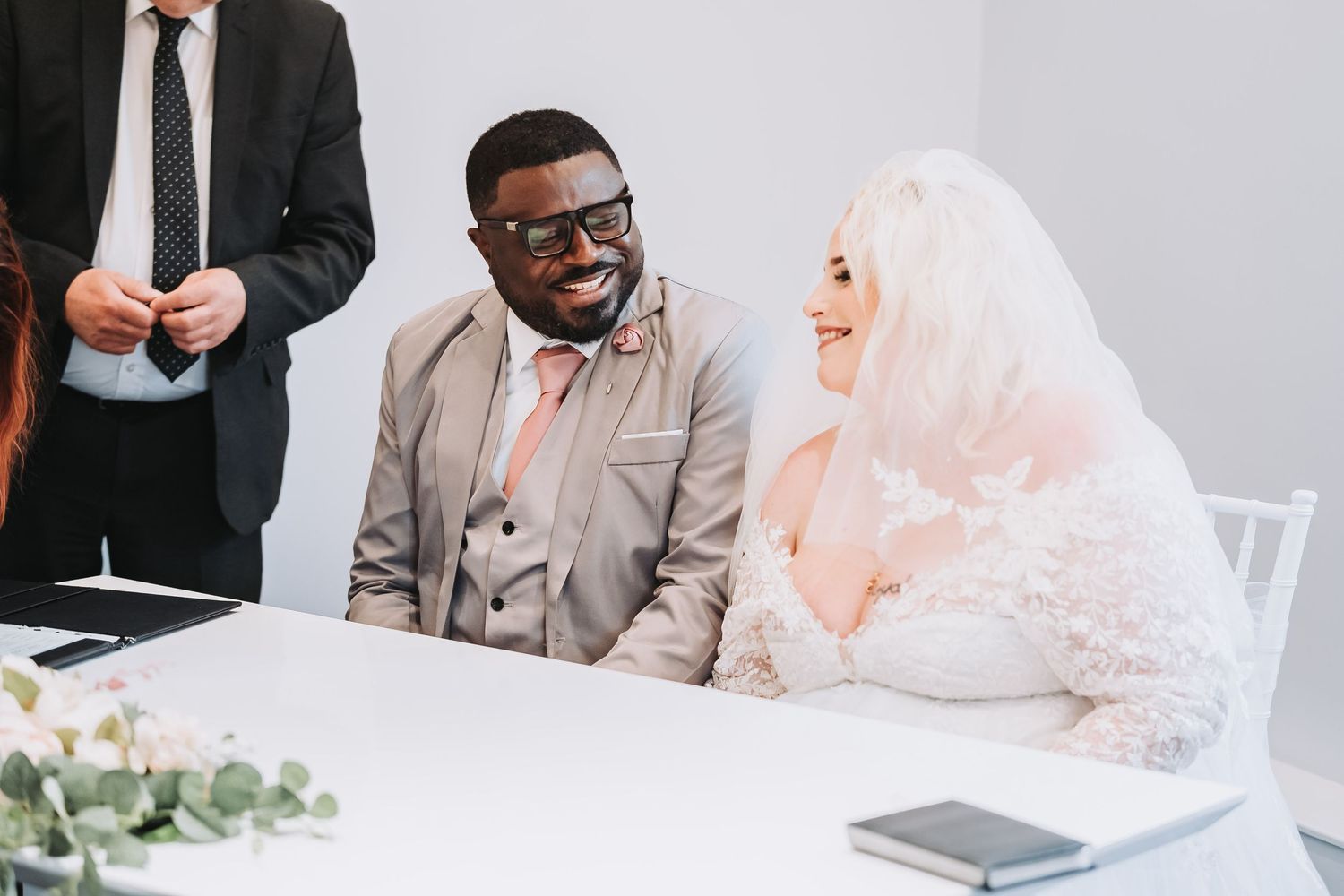 A couple shares a joyful moment at a wedding ceremony table decorated with greenery and white flowers taken at Chesterfield Register office