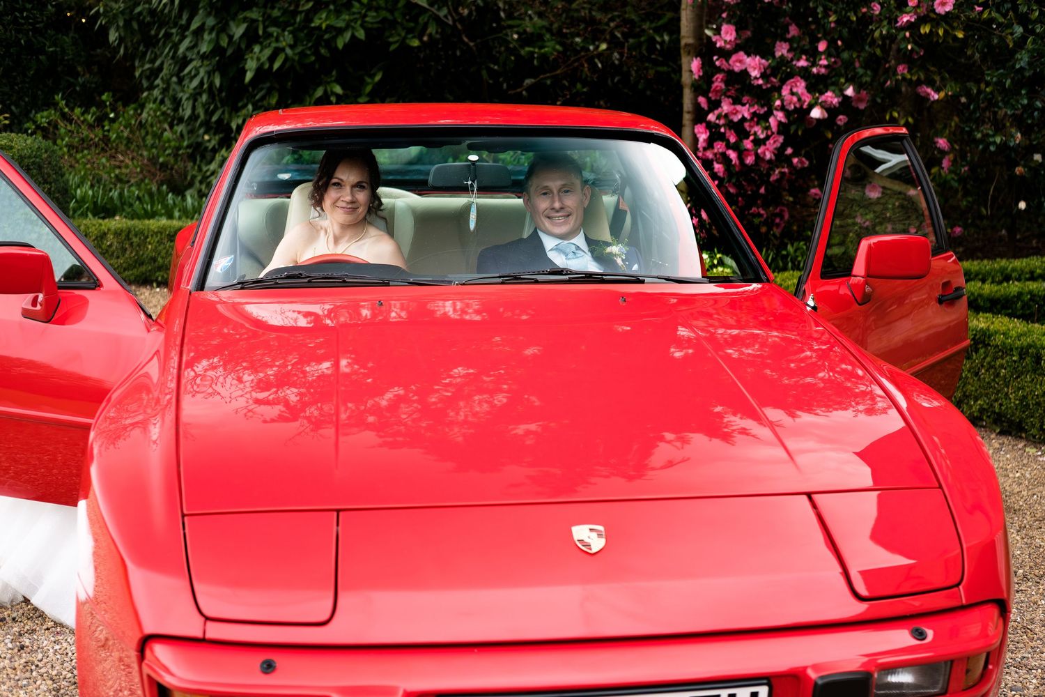 Bride and groom sitting in a classic red Porsche convertible on their wedding day.