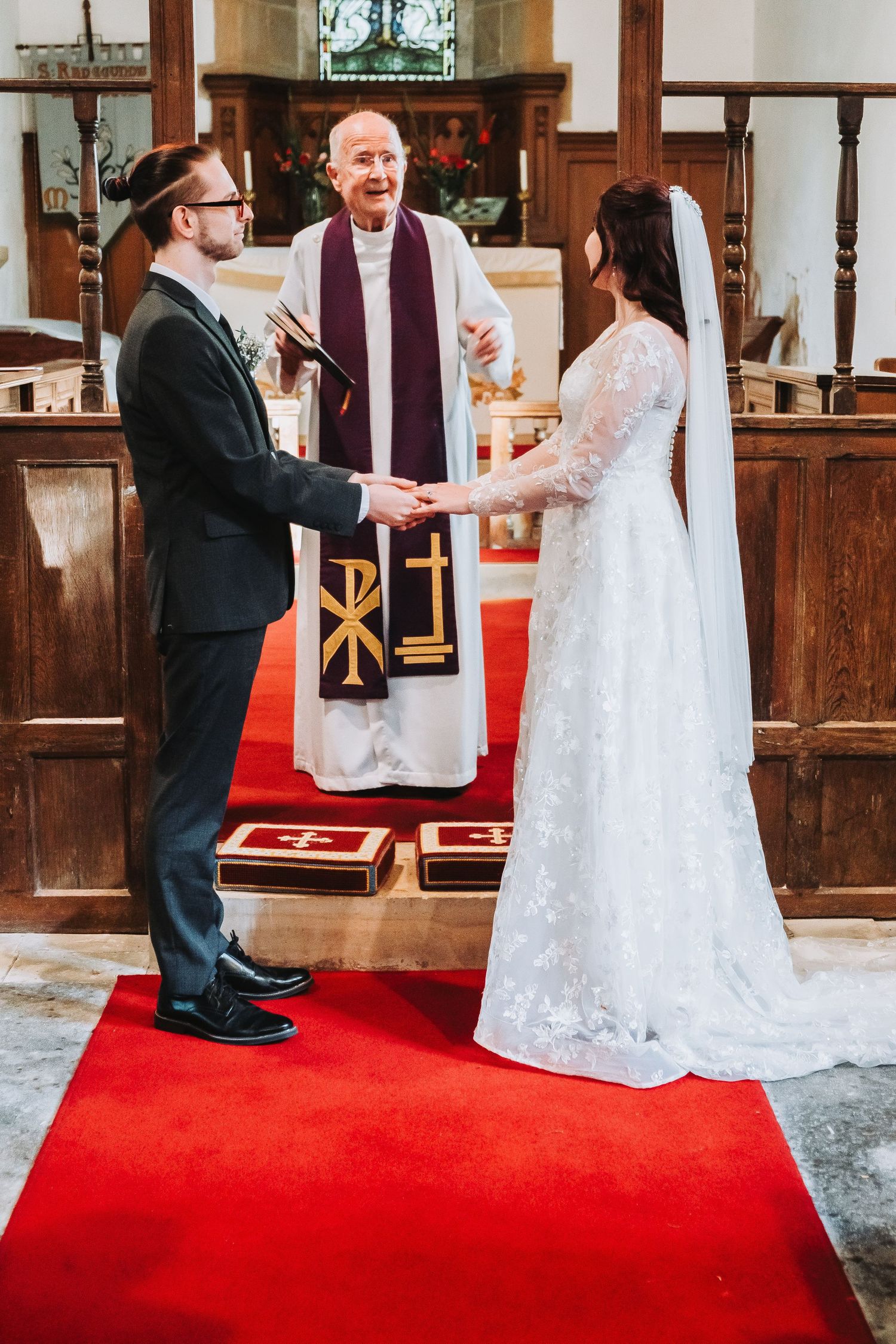 A couple shares a playful moment during their wedding ceremony on a red carpet in a church.