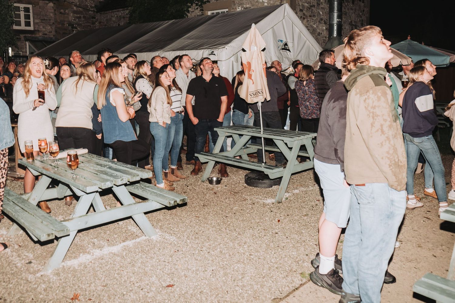 Large crowd gathered around picnic tables during an evening outdoor celebration.