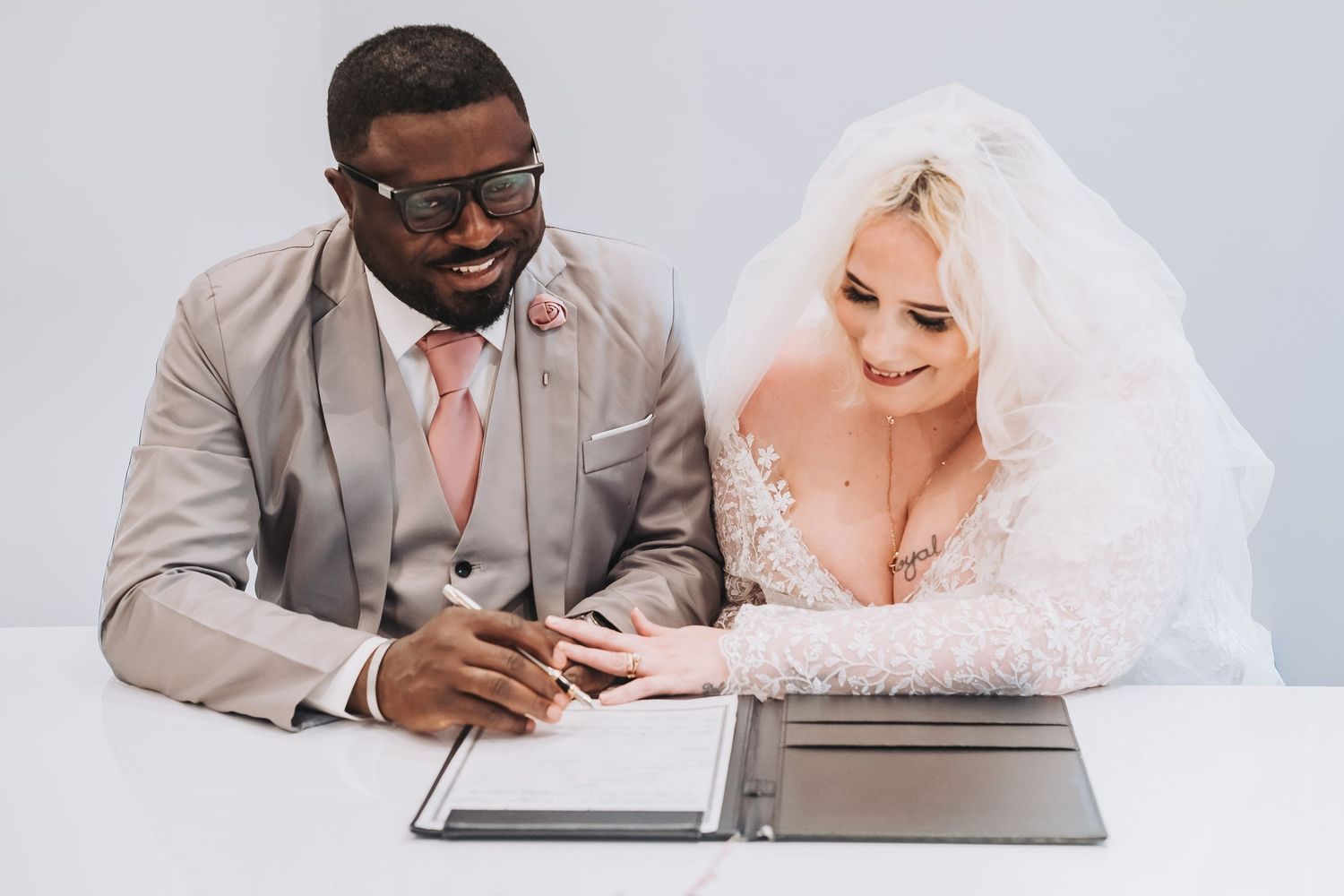 Couple reviews and signs marriage paperwork together at a modern desk.