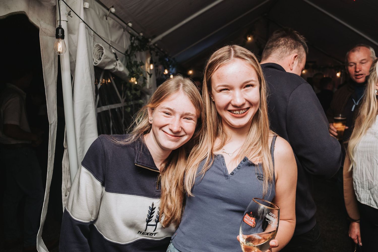 Friends celebrating at a party under a white tent with drinks and smiles.