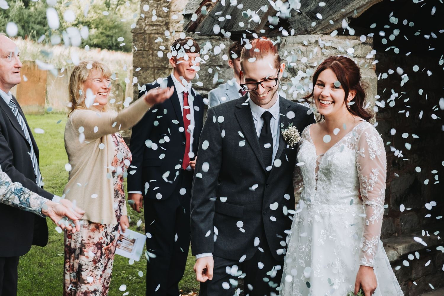 Wedding party celebrates with white confetti falling around them during outdoor celebration.