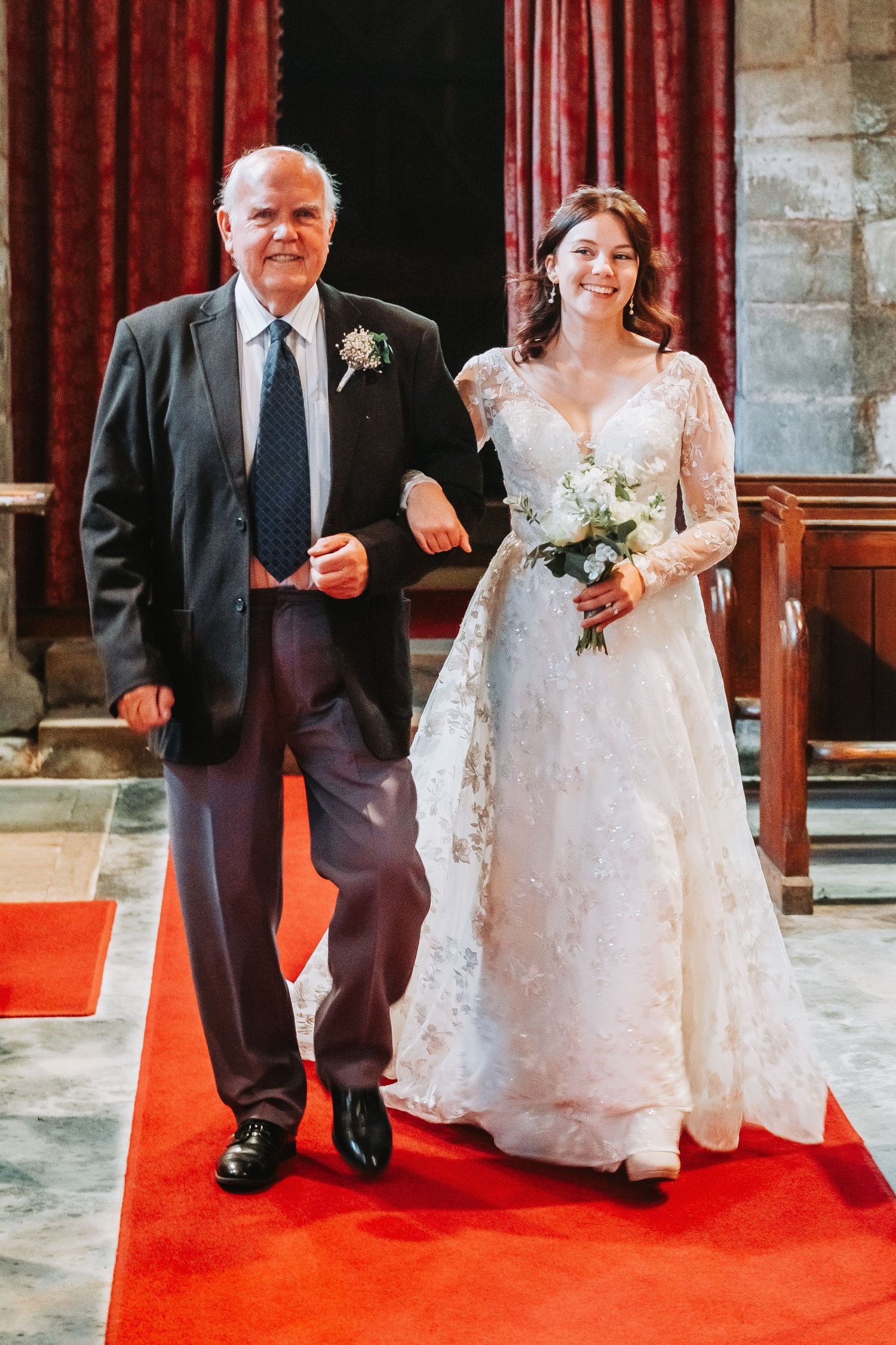 Wedding processional on red carpet shows couple walking down church aisle in traditional white gown and dark suit.