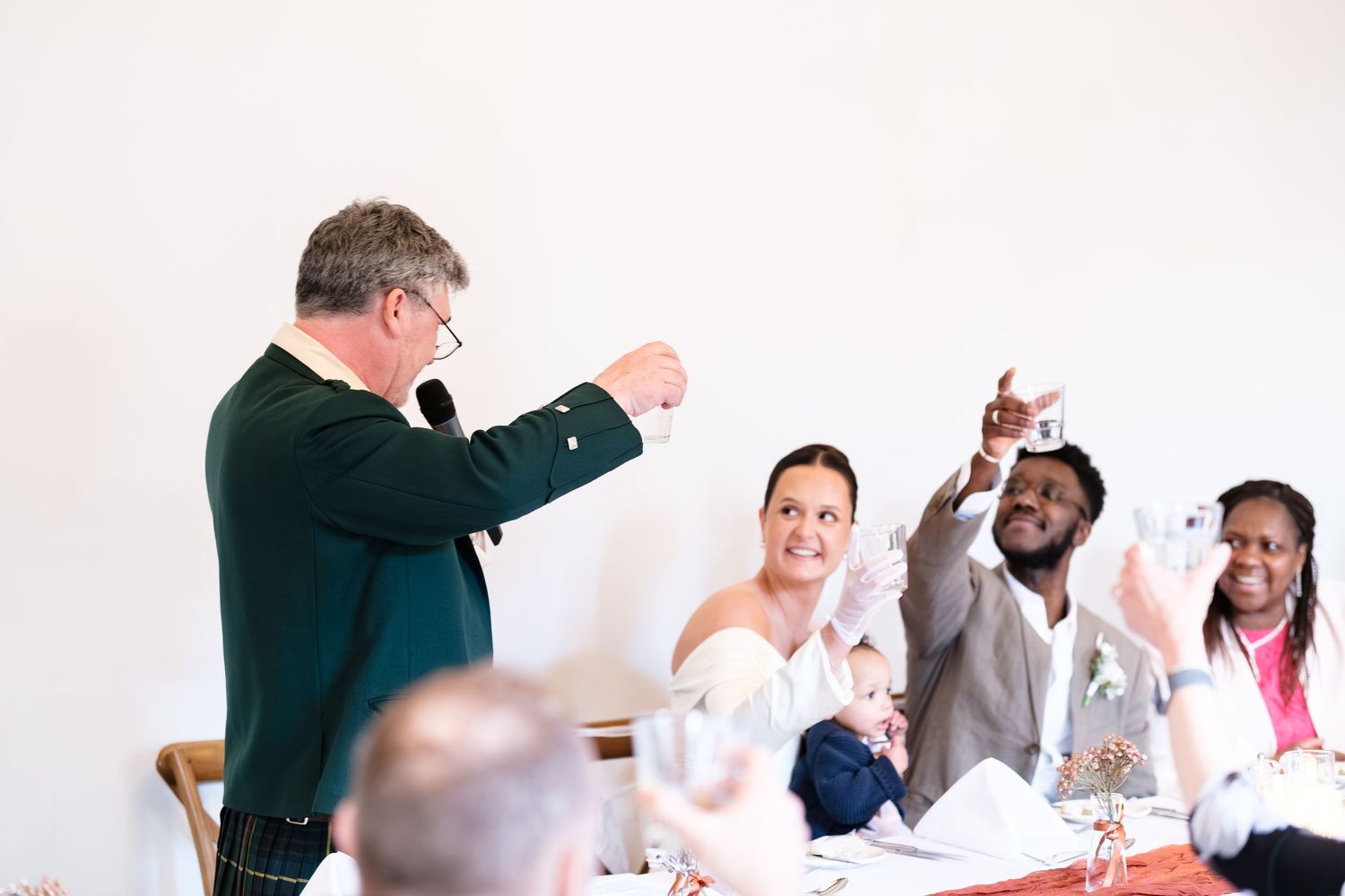 Wedding toast scene with guests raising glasses as a man in green jacket leads the celebration at a reception dinner at dunston hall estate