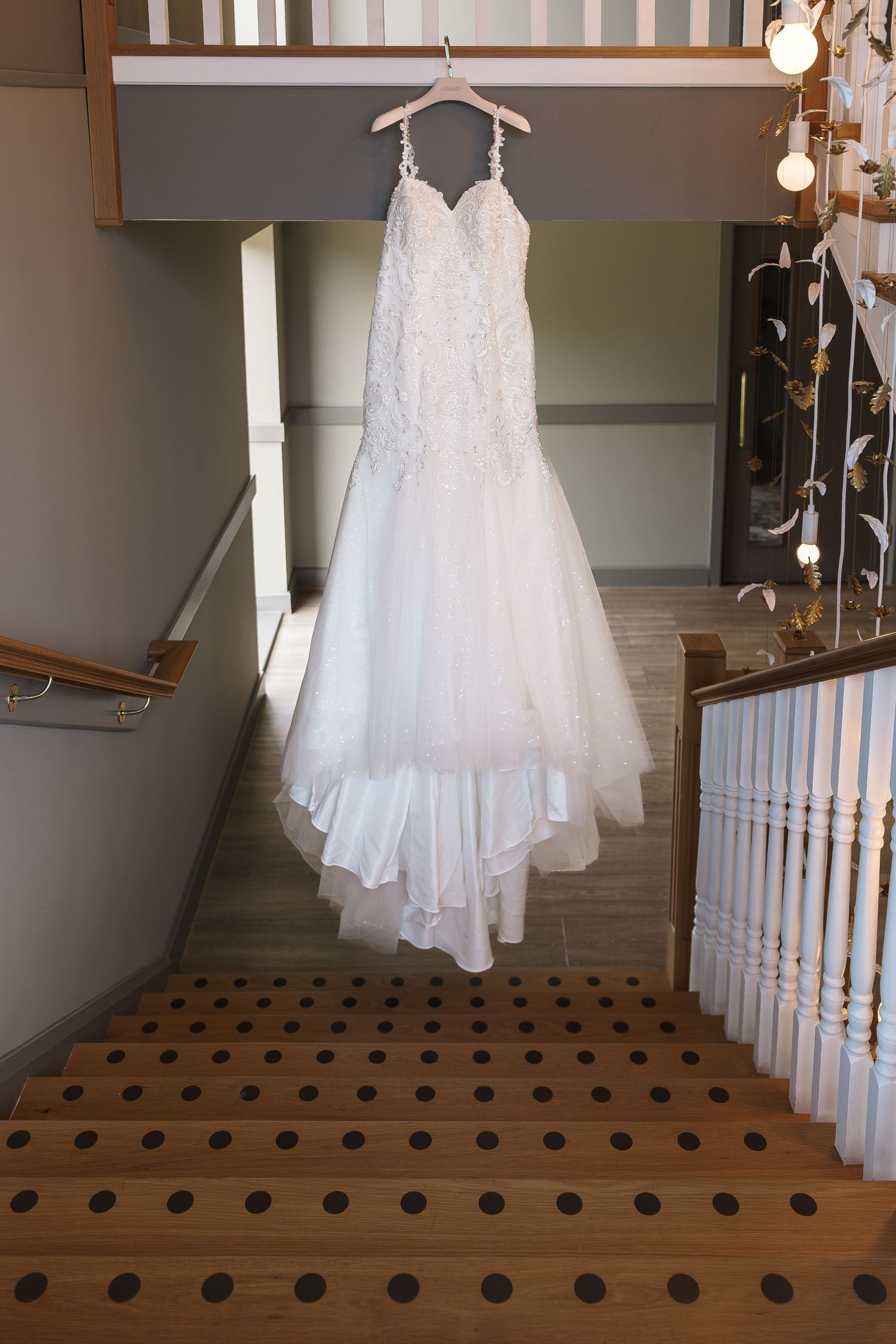 Elegant white lace mermaid wedding dress hanging on wooden staircase banister at Wildes Inn, Chesterfield taken by 21 Photography