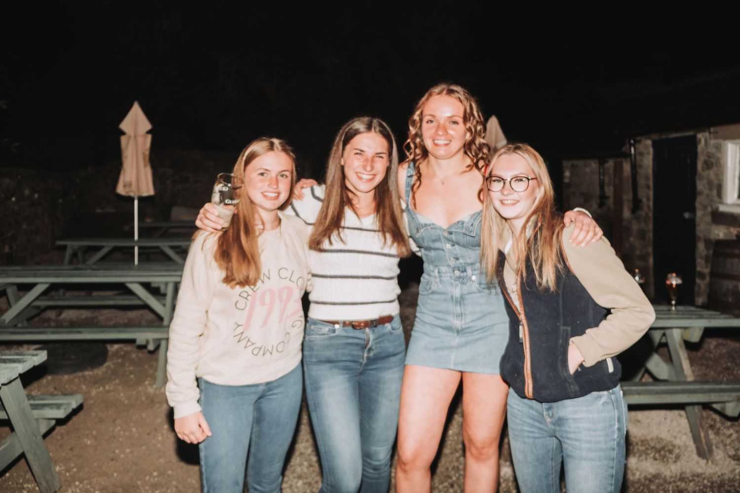 Group of friends posing together outdoors at night on wooden picnic tables.