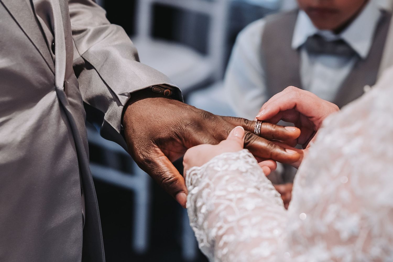 Close-up of hands adjusting a white lace wedding dress fastener on a bride's back.