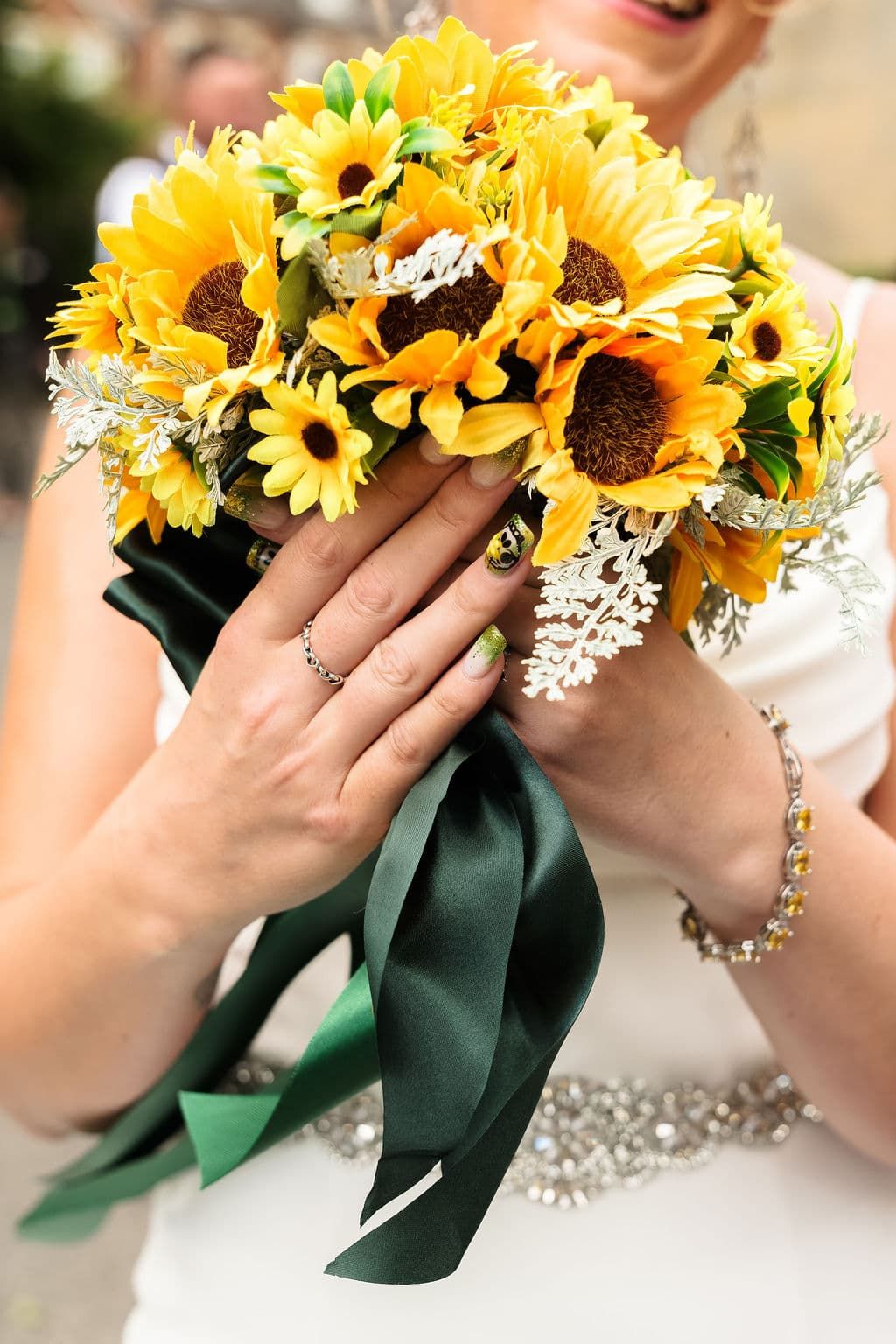 Bride holding a vibrant sunflower wedding bouquet with green satin ribbon, wearing a diamond ring and bracelet taken by 21 photography