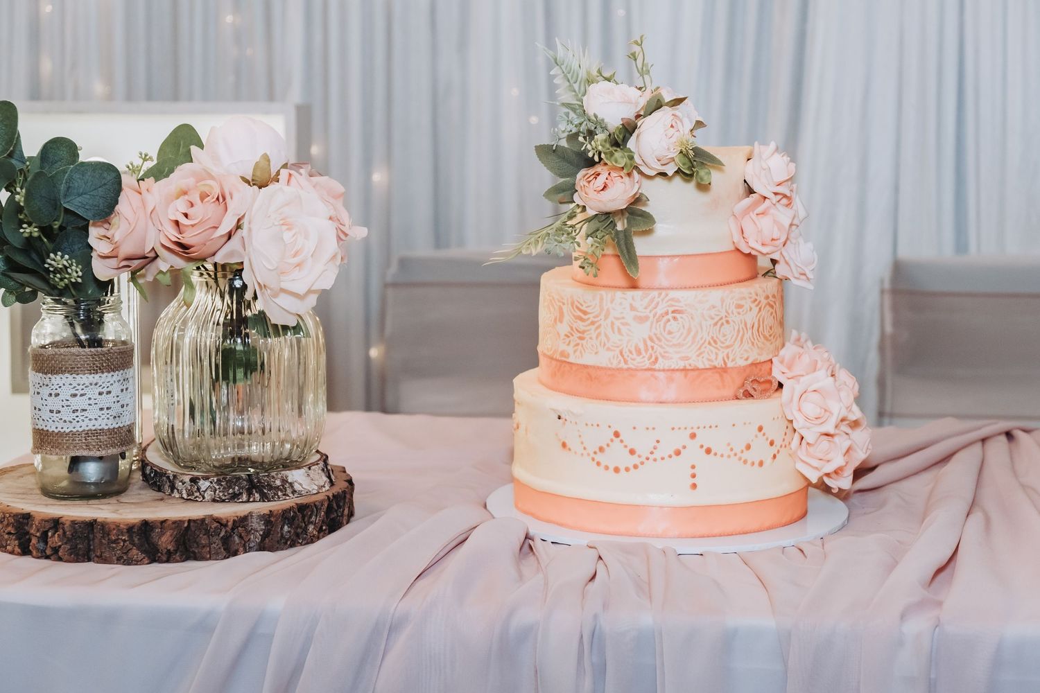 Row of elegant wedding cakes with peach and blush details displayed on rustic wood slices.