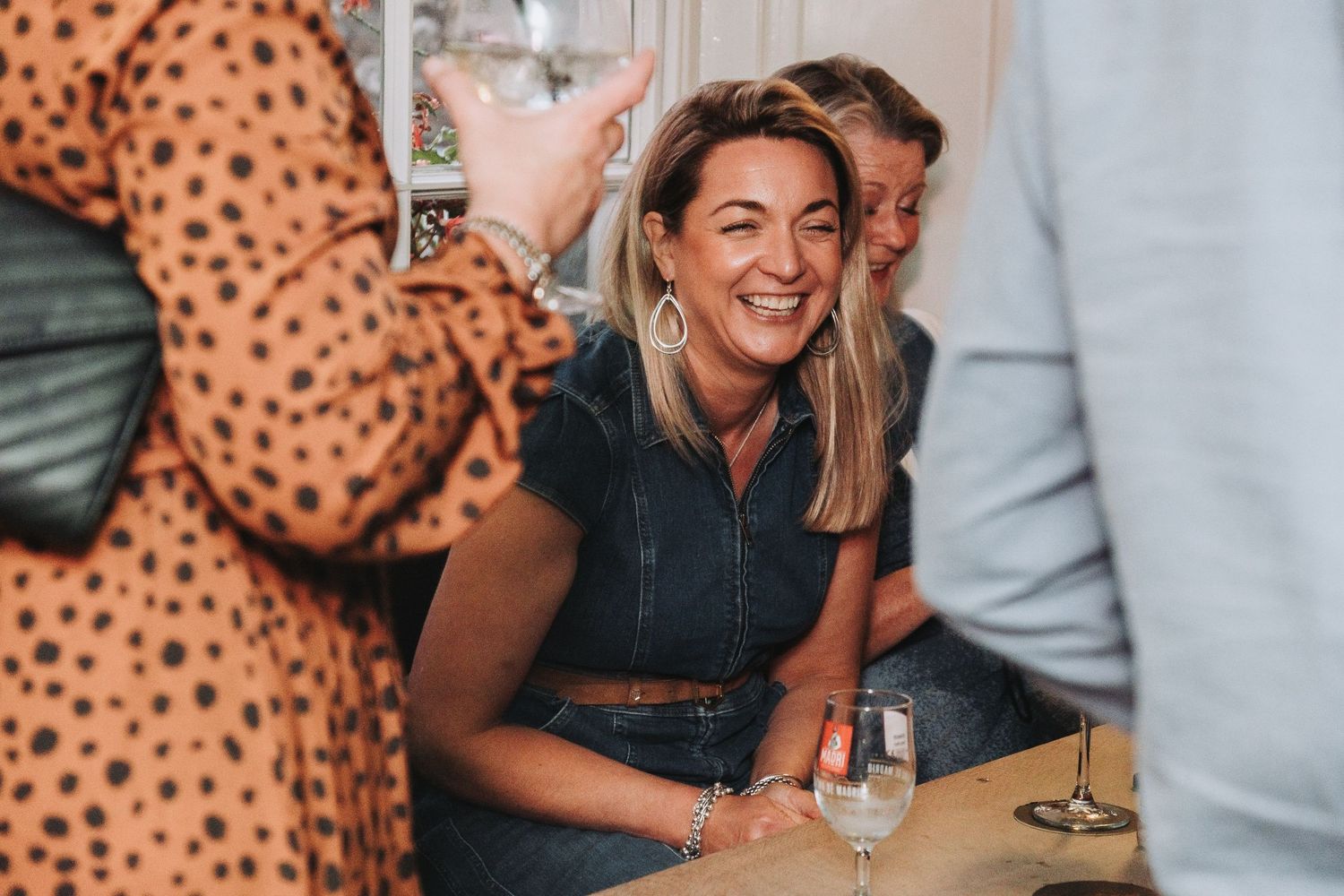A candid moment captures someone laughing while seated at a social gathering with friends and drinks.
