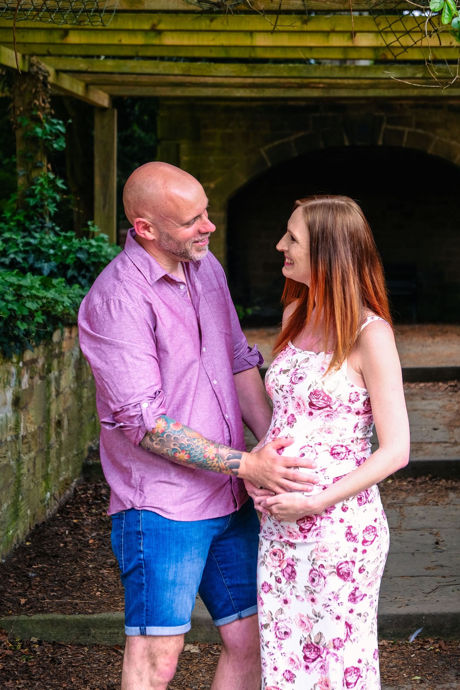 Couple in casual attire standing under rustic wooden pergola during outdoor photoshoot.