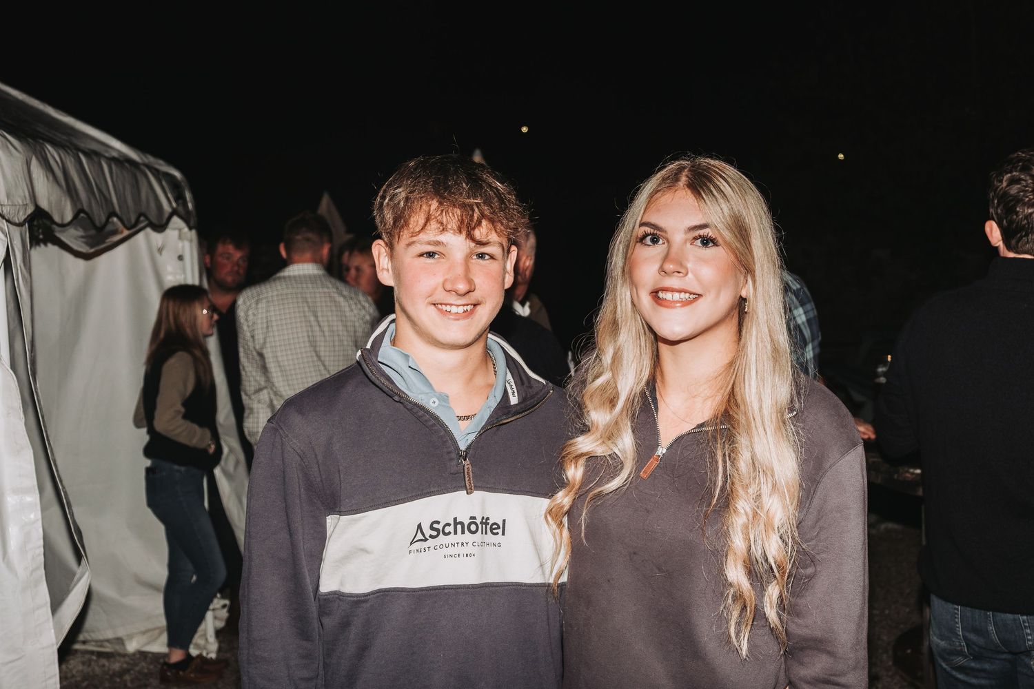 A couple enjoying a nighttime event under a tent structure.