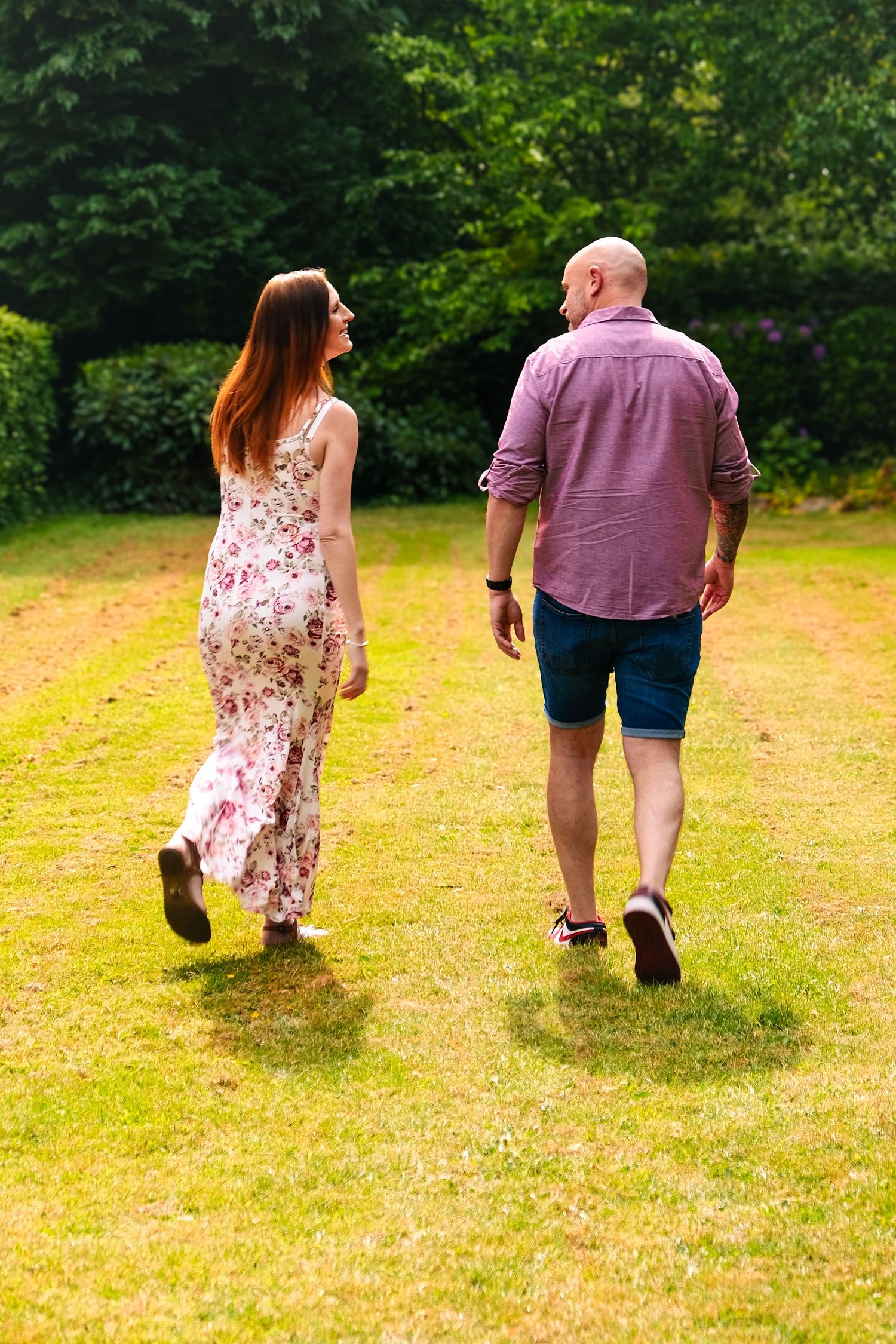 Couple walking away together on a sunny yellow grass field.