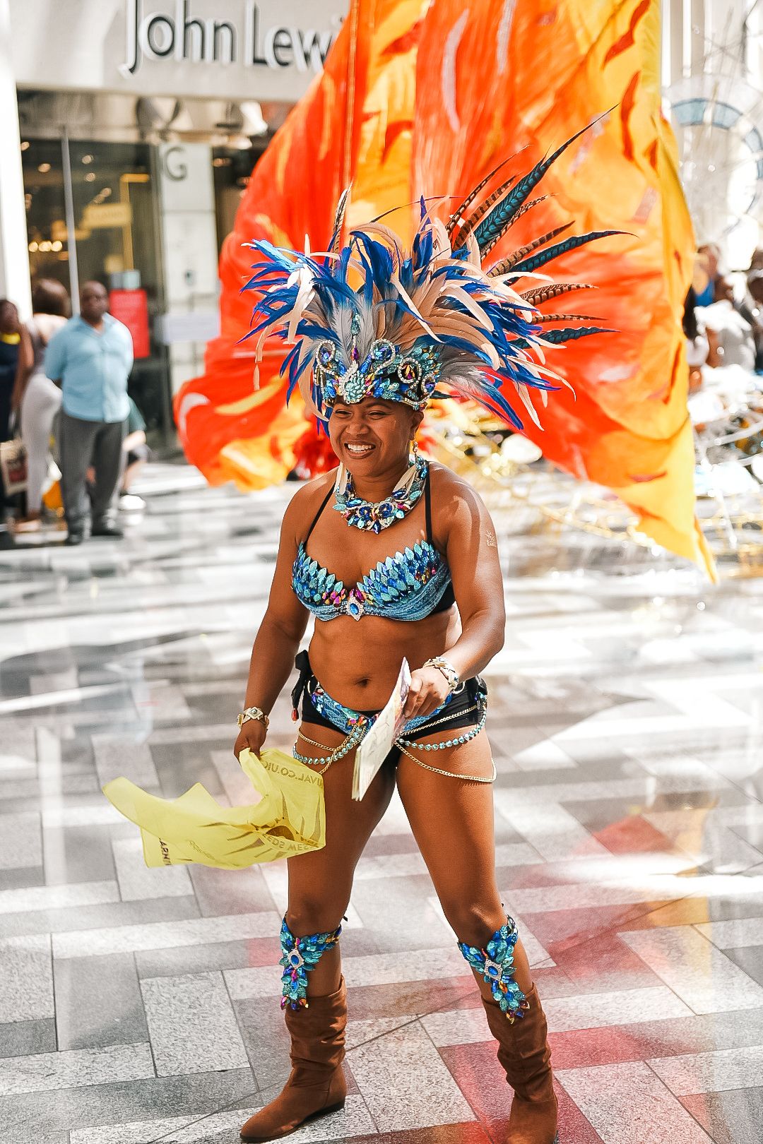 Carnival performer in vibrant blue and orange feathered costume at John Lewis storefront shot in Leeds by 21 Photography