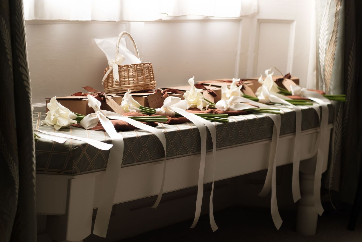 Elegant wedding table display with white ribbon-tied floral arrangements and a wicker basket centerpiece on a draped table  at dunston hall