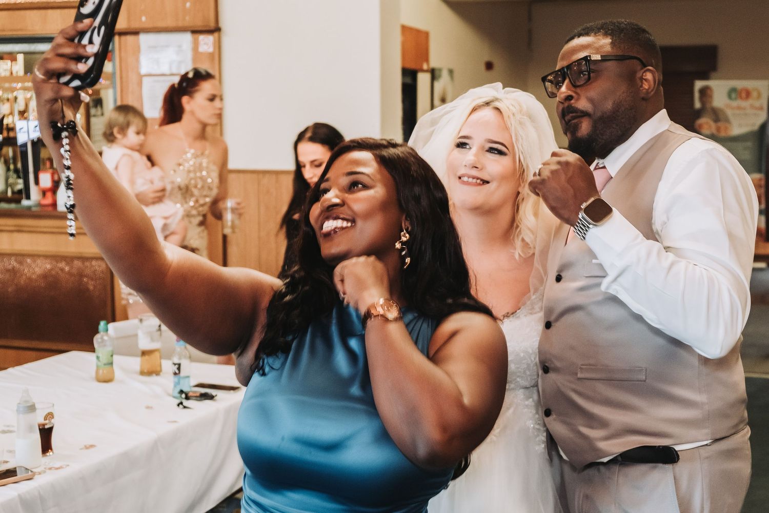 Wedding guests taking selfies and celebrating during lively reception party.