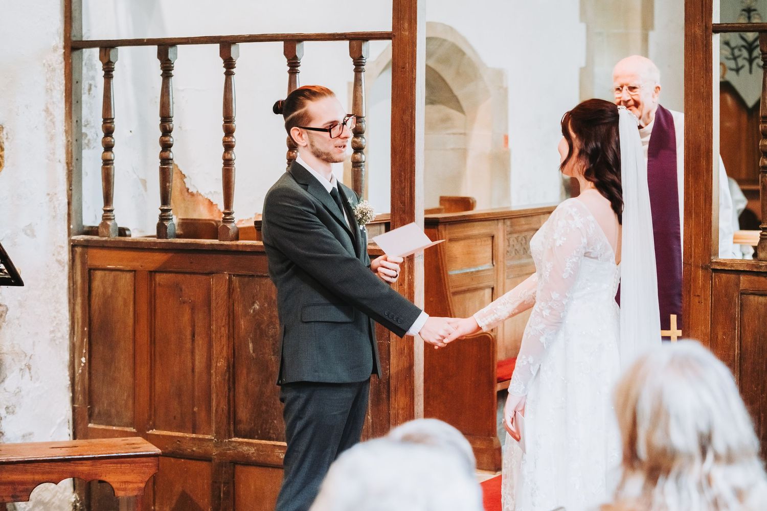 A romantic wedding ceremony takes place inside a traditional church with wooden pews and red carpet.