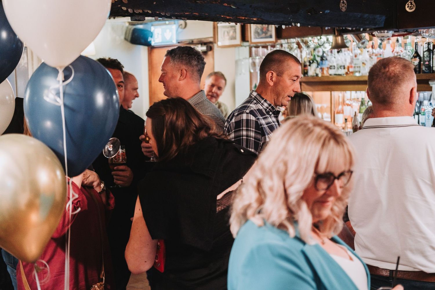 Guests socialize and mingle at a lively party venue with colorful balloons and ambient lighting.