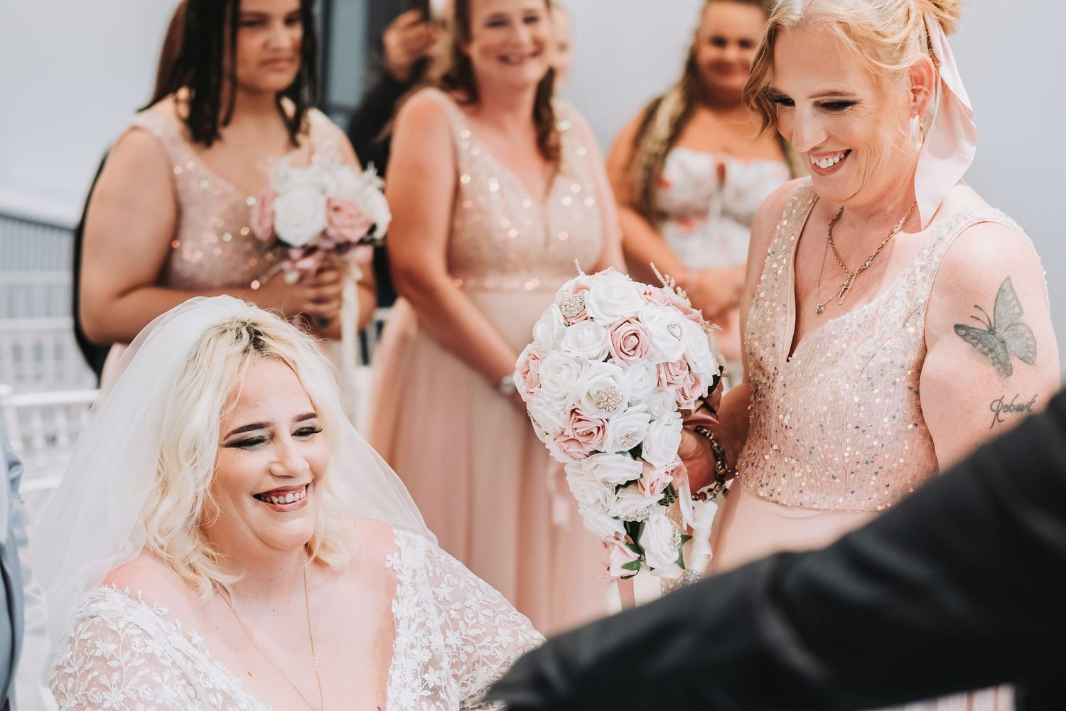 Bridesmaids wearing blush pink dresses smile during a wedding celebration.