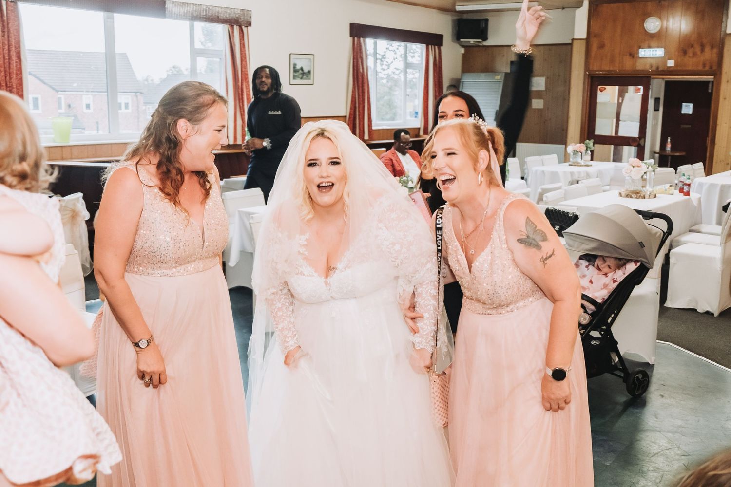 Wedding party in blush pink dresses gather together in an indoor venue for group photos.