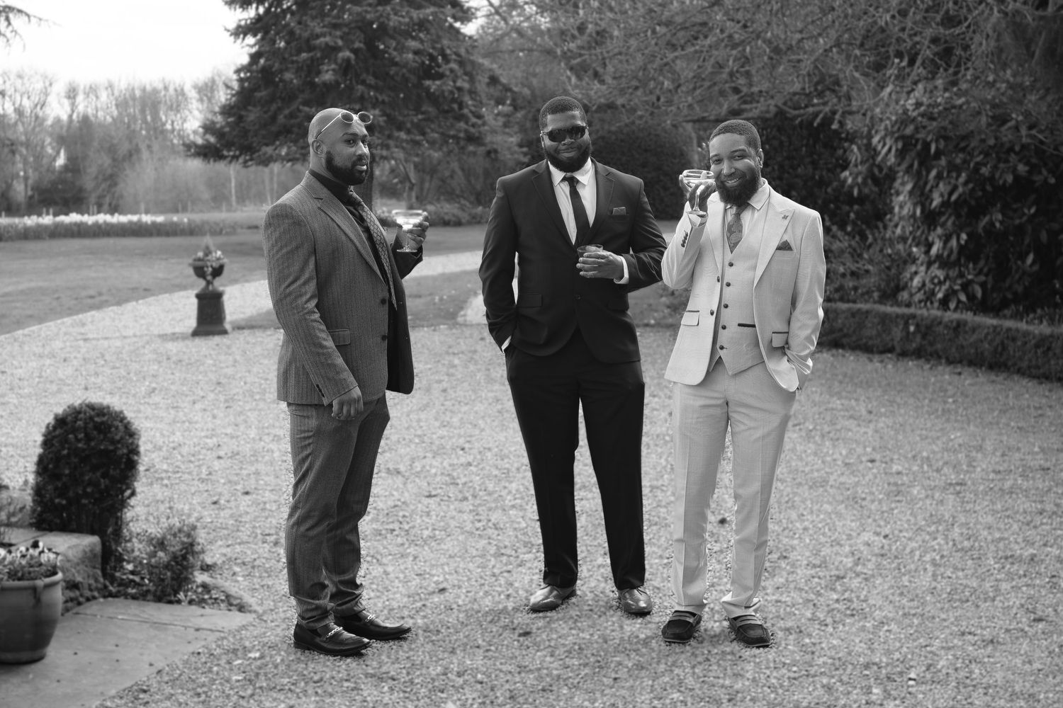 Three well-dressed men in suits socializing outdoors in a black and white photo at a formal garden event.
