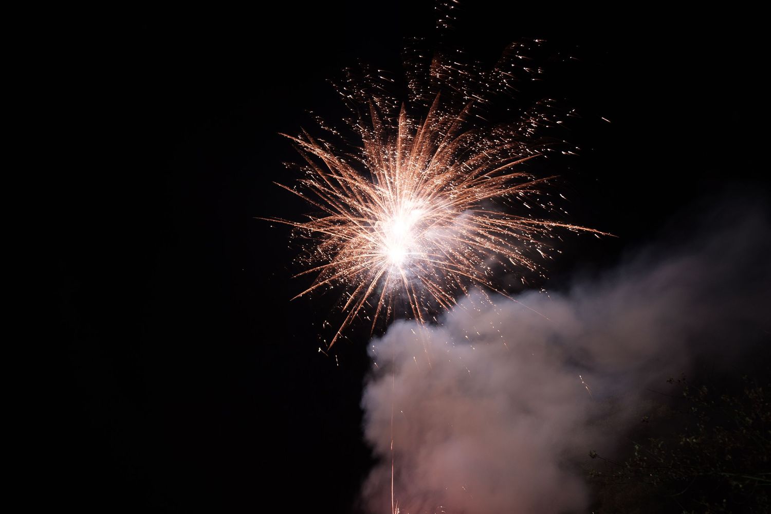 Bright fireworks exploding against a dark night sky with smoke trails visible.