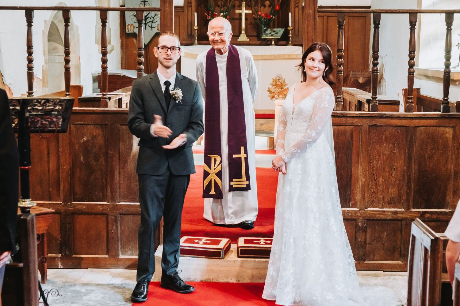 Wedding ceremony taking place inside a traditional church with wooden paneling and red carpet.