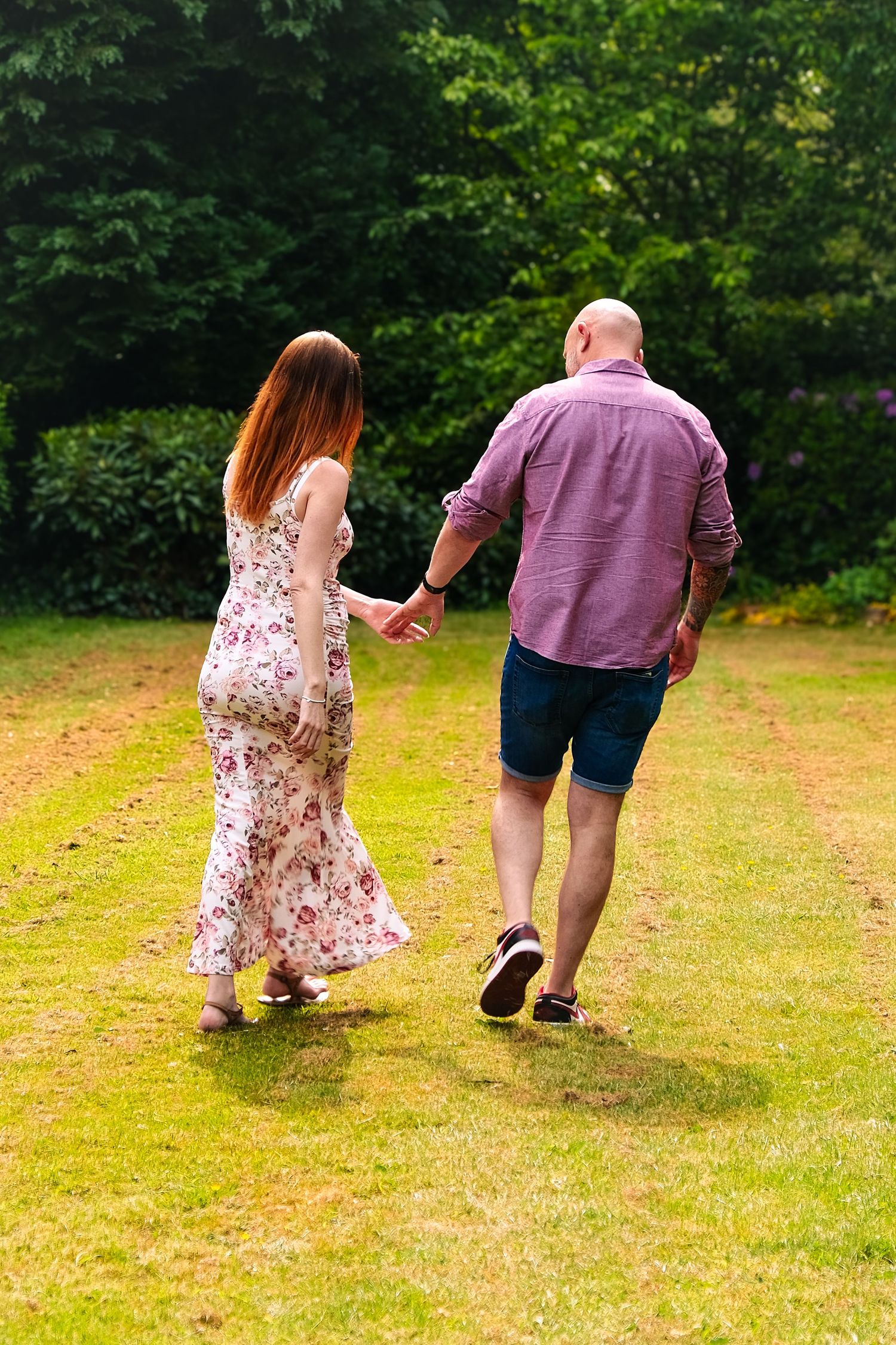 People walking on grass with green trees in background, wearing casual summer attire.