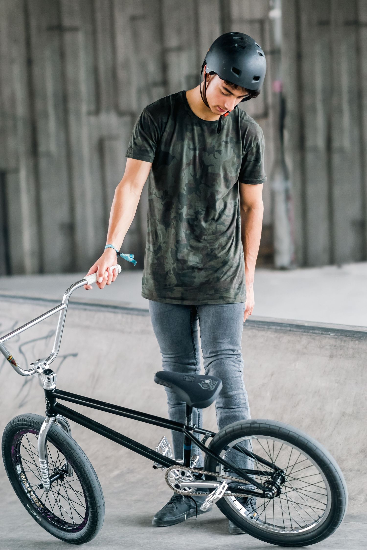 BMX rider stands with black bike in indoor skate park wearing protective helmet shot in Leeds by 21 Photography