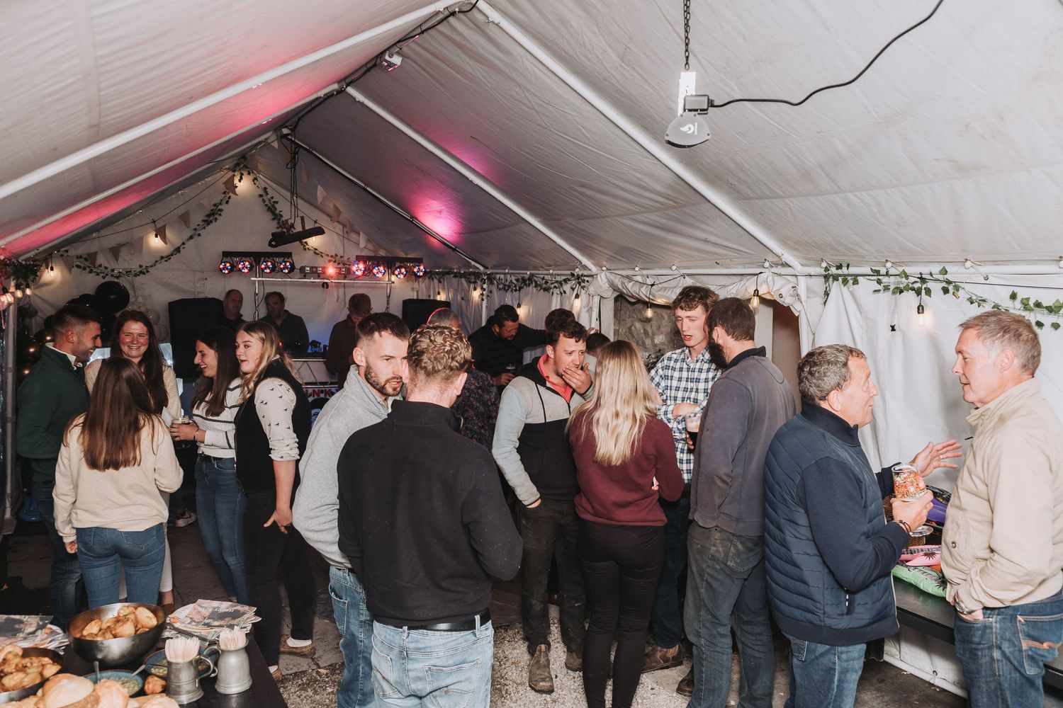 Crowded party scene under a white tent with pink lighting and people mingling.