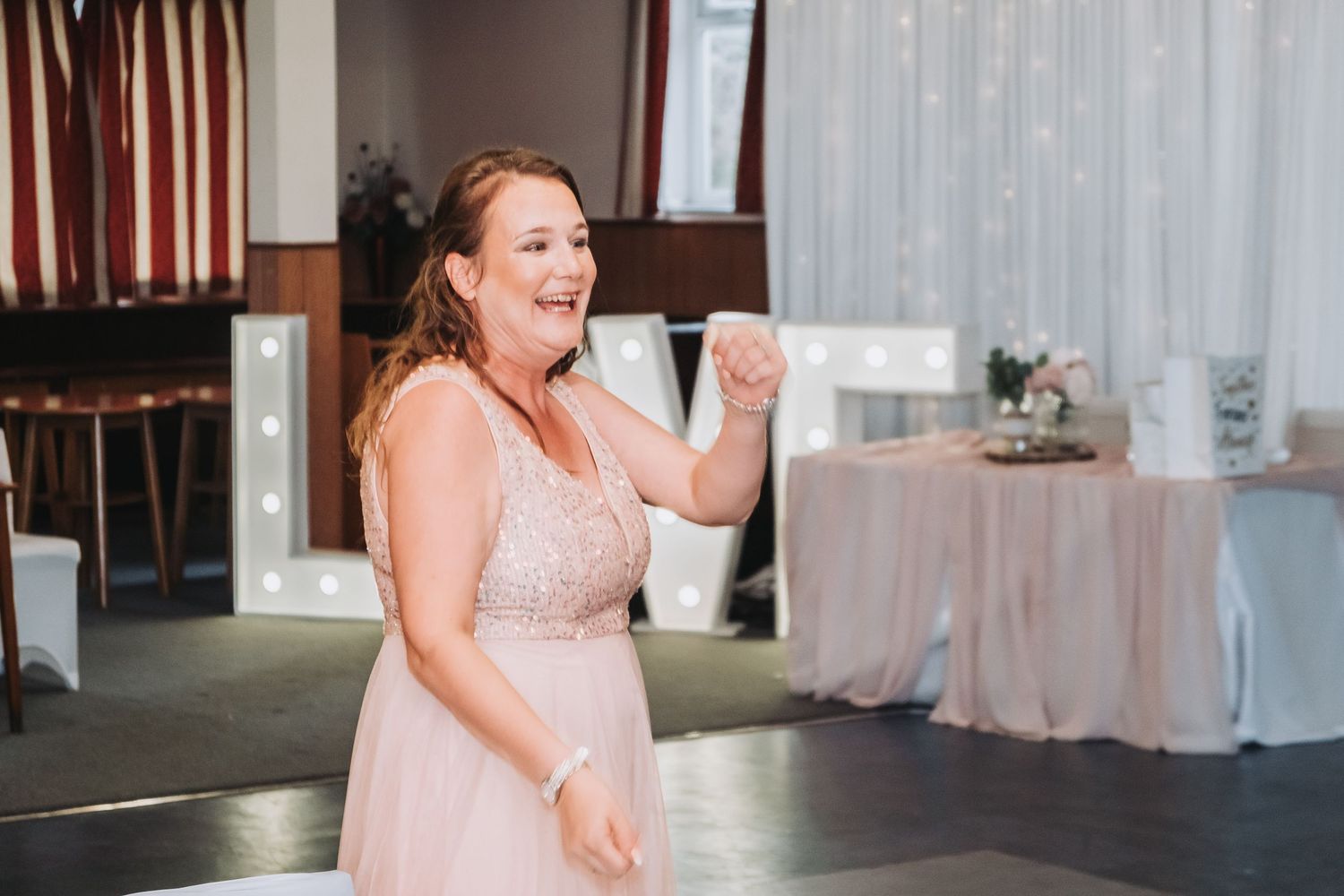 Person in elegant blush gown spins gracefully on the dance floor at an indoor reception venue.