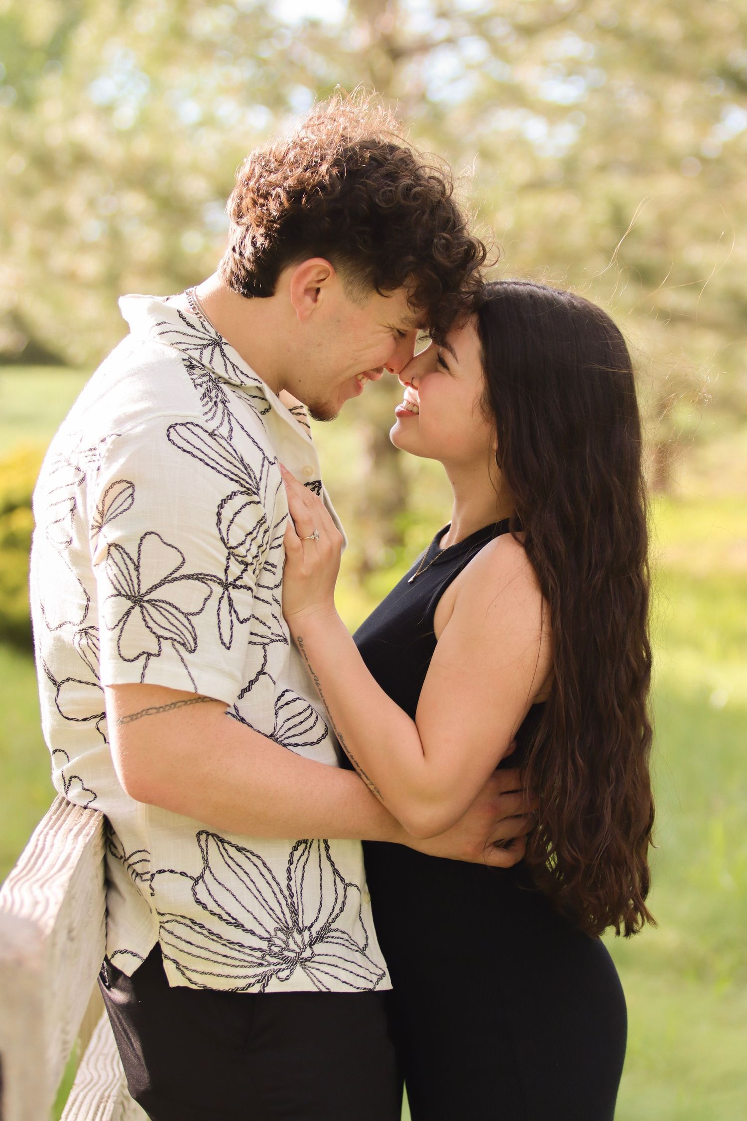 Young couple sharing a romantic moment outdoors, touching foreheads in a sunny green park setting.