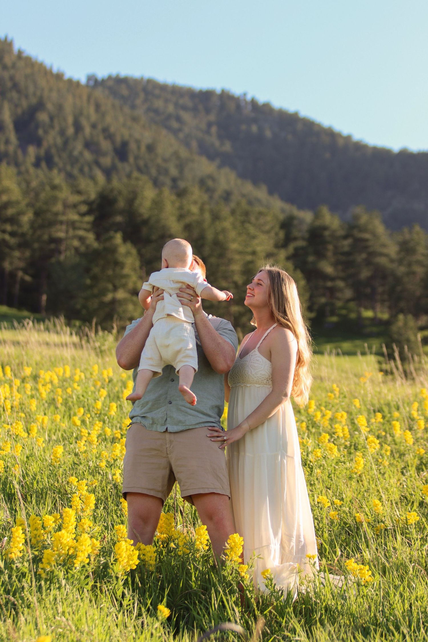 Family with baby in yellow flower field, mountains in background, golden hour light.