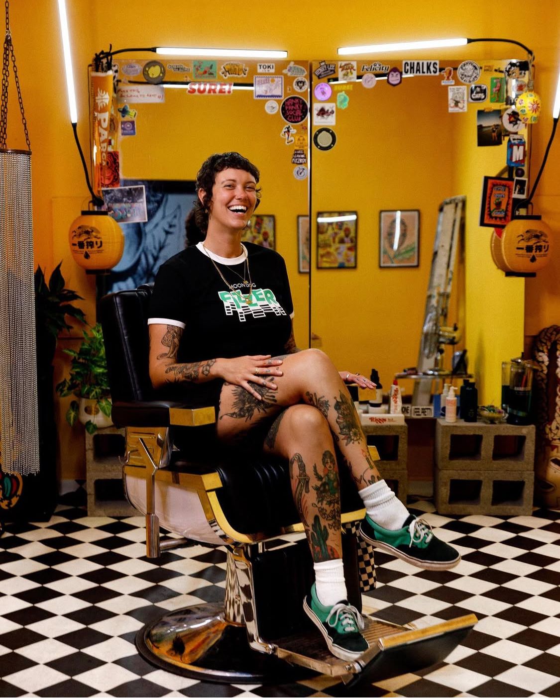 Person sitting in a checkered floor barbershop with yellow walls and vintage decor displayed on the walls. By Chapter Portraits Melbourne