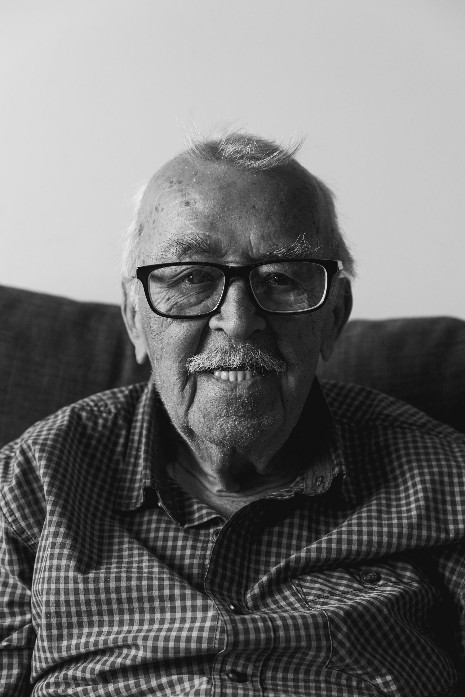 Black and white portrait showing an elderly person in glasses and checkered shirt smiling warmly taken by Chapter Portraits Melbourne
