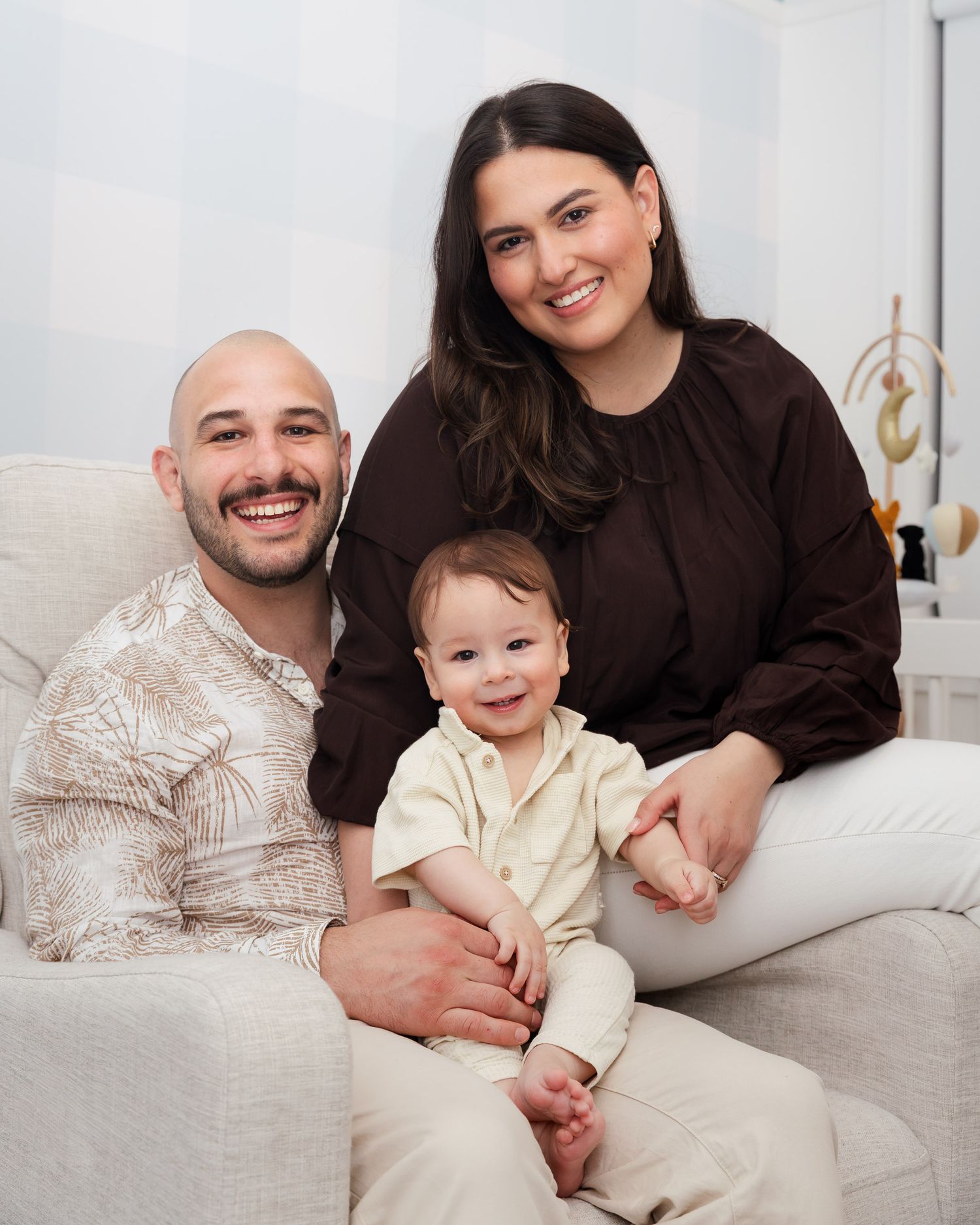 A family wearing brown and beige outfits poses together on a white couch for a professional photo shoot.