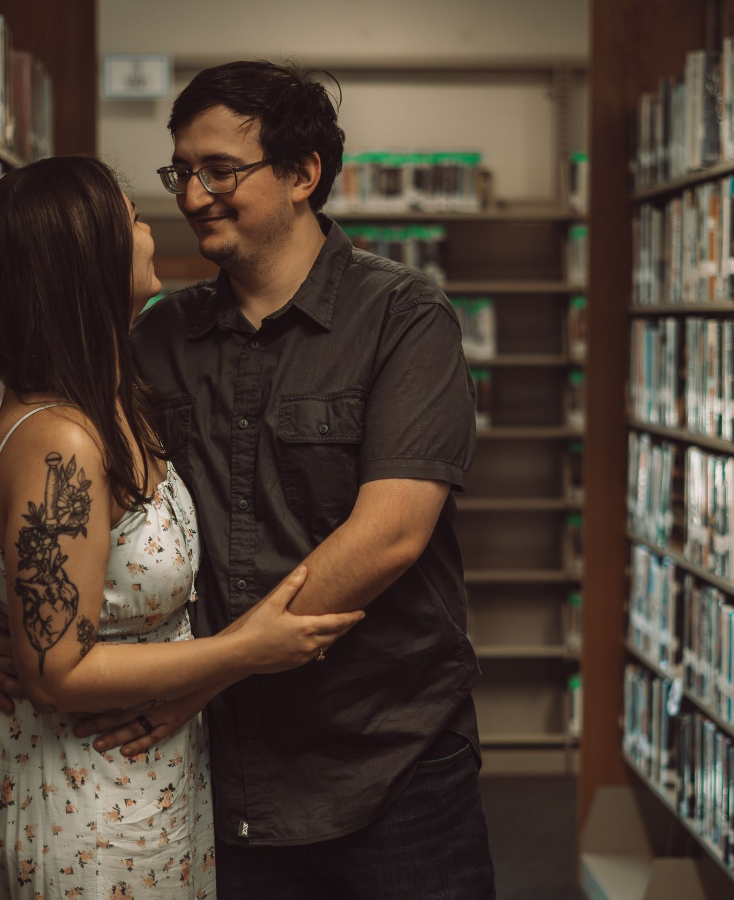 A couple embraces while standing between library bookshelves.