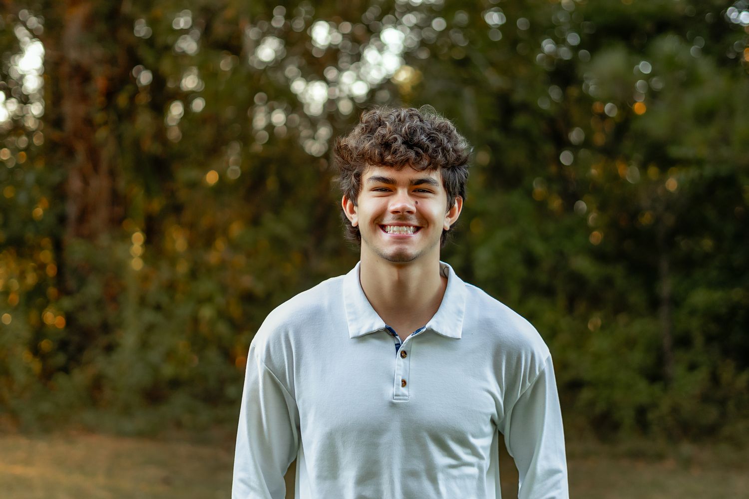Portrait of a student in white polo shirt smiling outdoors.