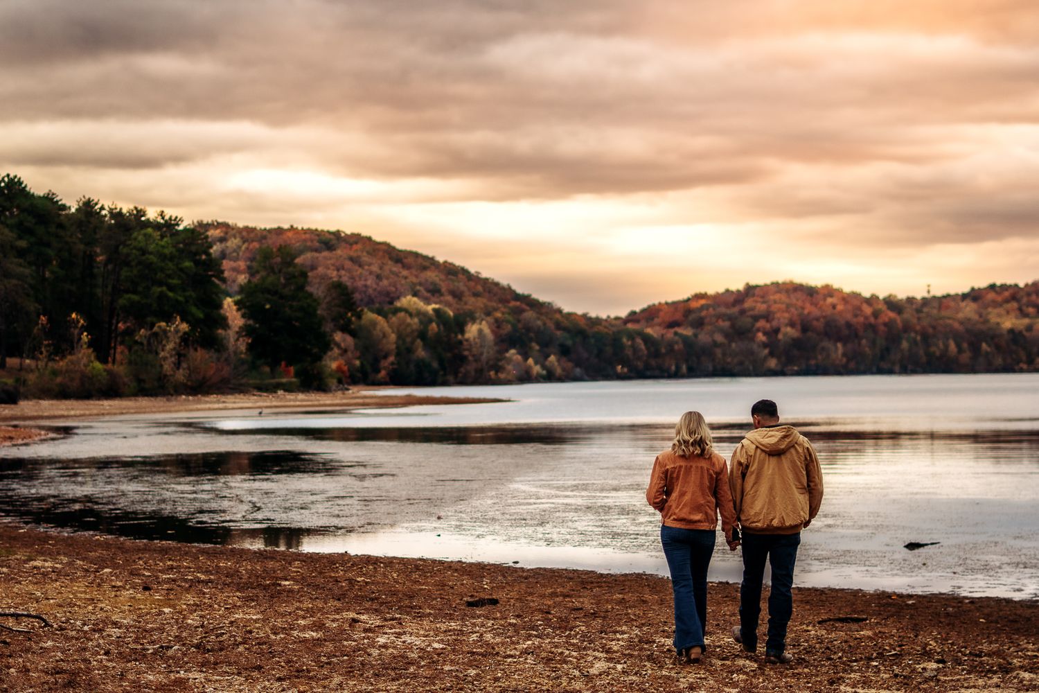 A couple walks along a scenic beach at sunset with dramatic orange and purple skies over the coastline.
