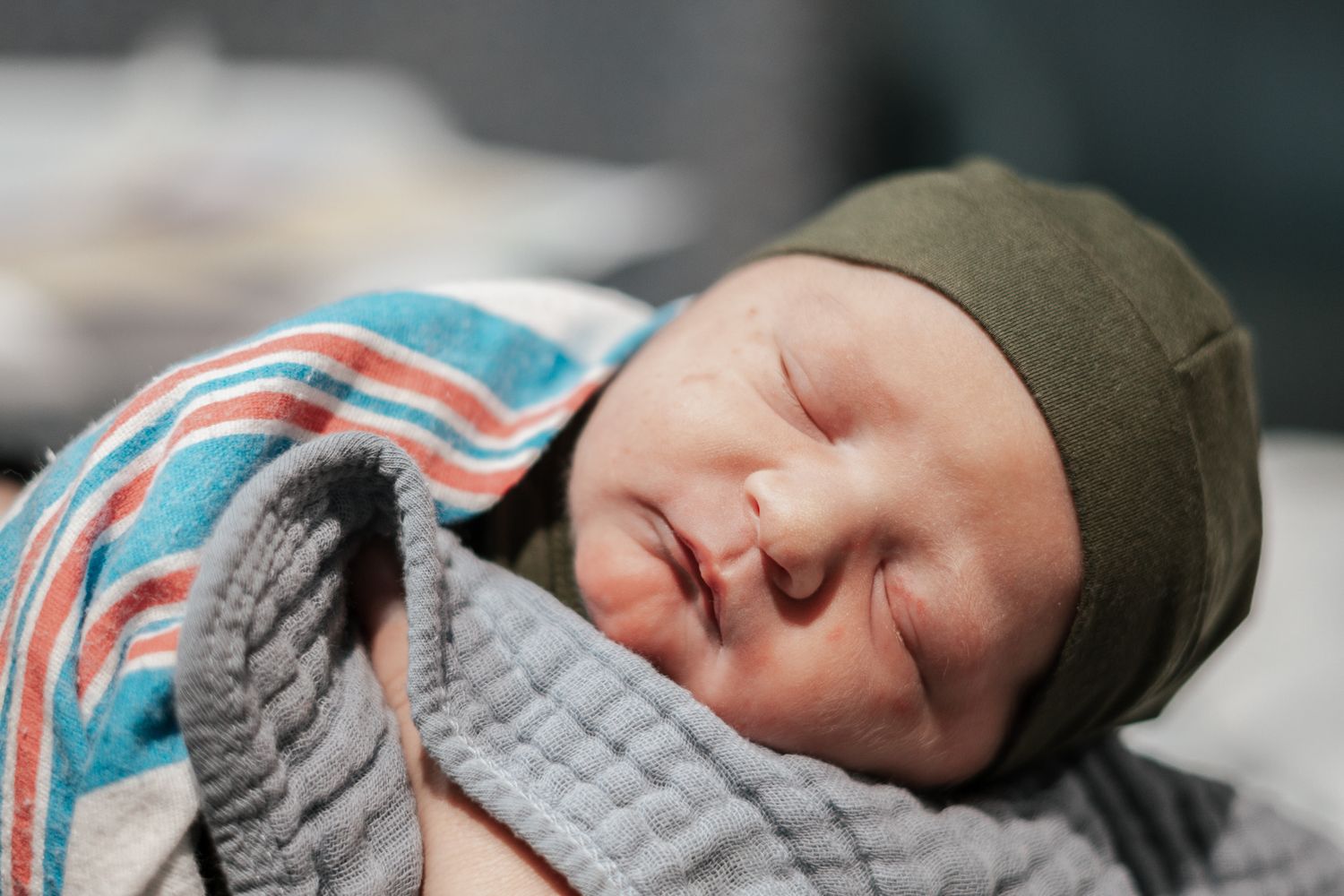 Sleeping infant wearing a cozy hat and striped blanket.